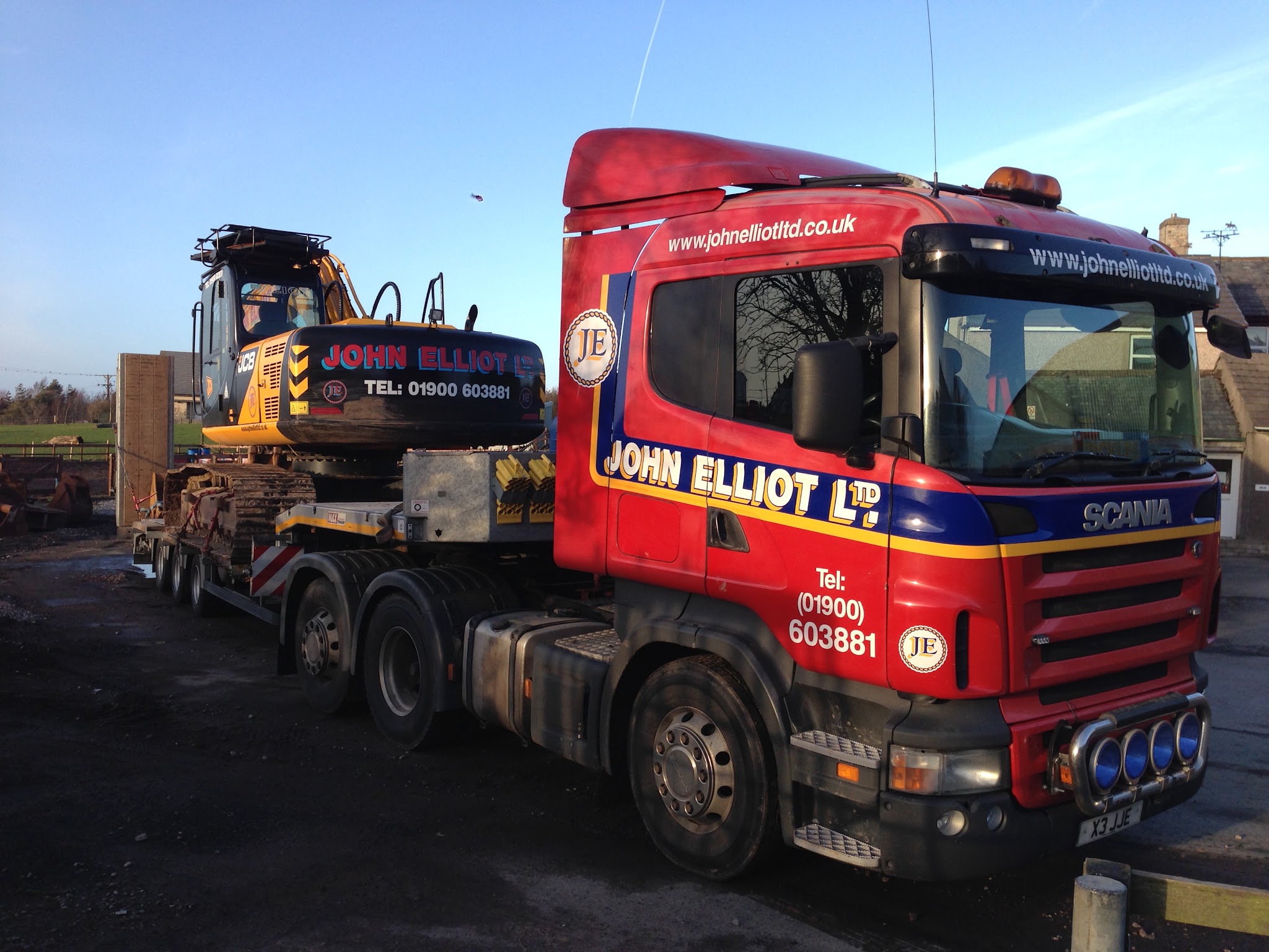 Red Scania tractor unit in John Elliot Ltd livery carrying a tracked excavator on the low loader