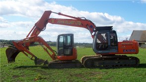 Orange tracked excavator lettered John Elliot Ltd on a grass site
